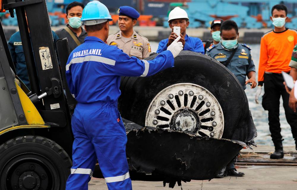 A worker assists his colleague during the lift up of a damaged tyre from the Lion Air flight JT610 jet