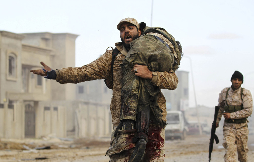 No end in sight: A member of the Libyan National Army carries an injured comrade during fighting against jihadists in Qanfudah