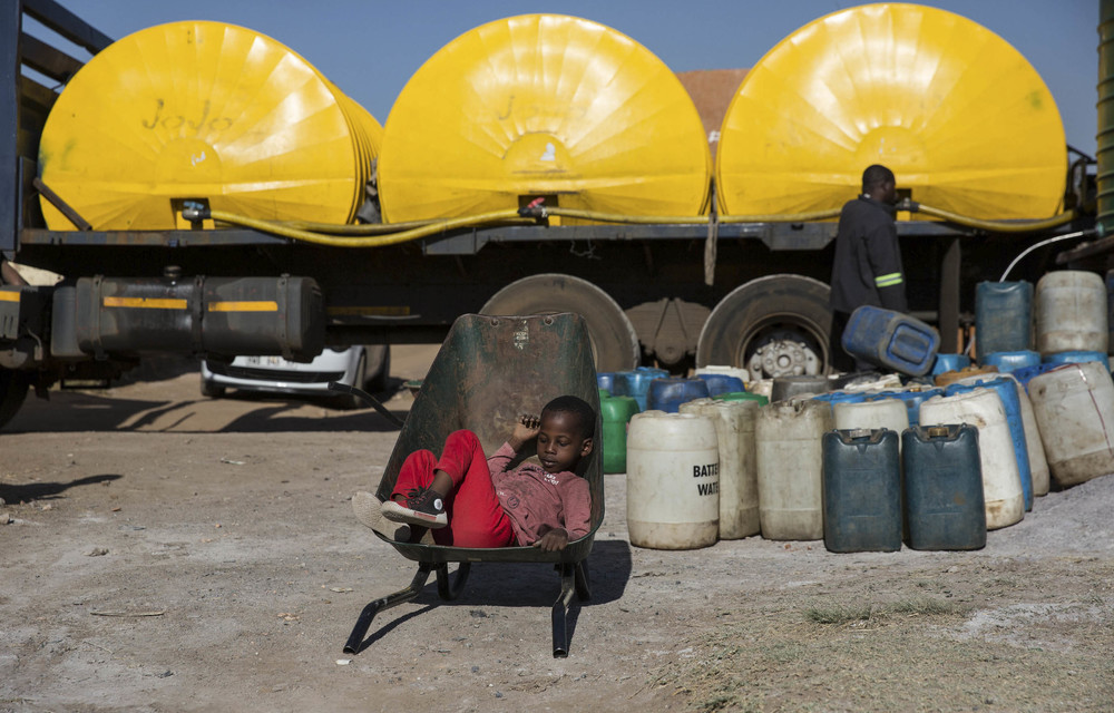 Six-year-old Malume Mashilo waits in the wheelbarrow his siblings will use to transport containers of water from a tank that has just been filled.