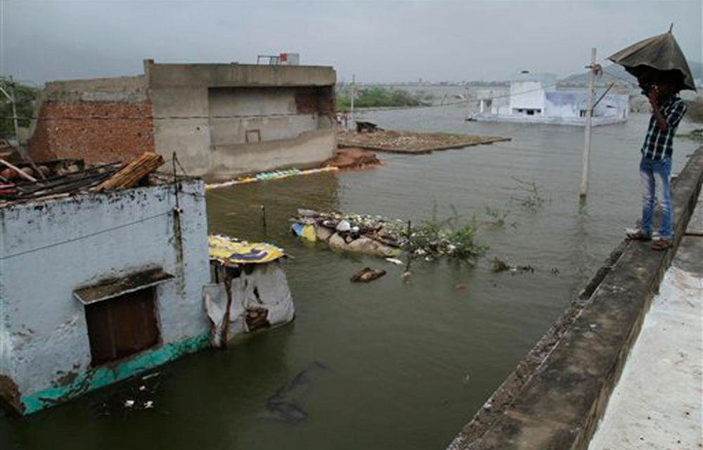 A youth holds an umbrella as he stands in a residential area that was partly submerged due to the overflowing of the Anasagar Lake after heavy monsoon rains in Ajmer