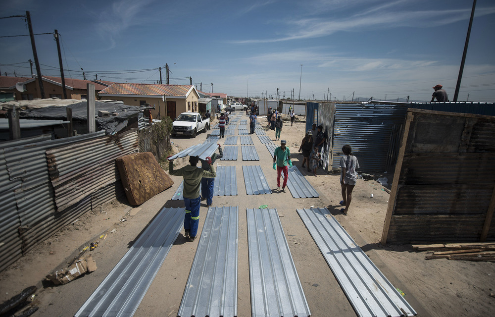 Residents receive a new shack building kit which comprises zinc sheets and other bits laid side by side.