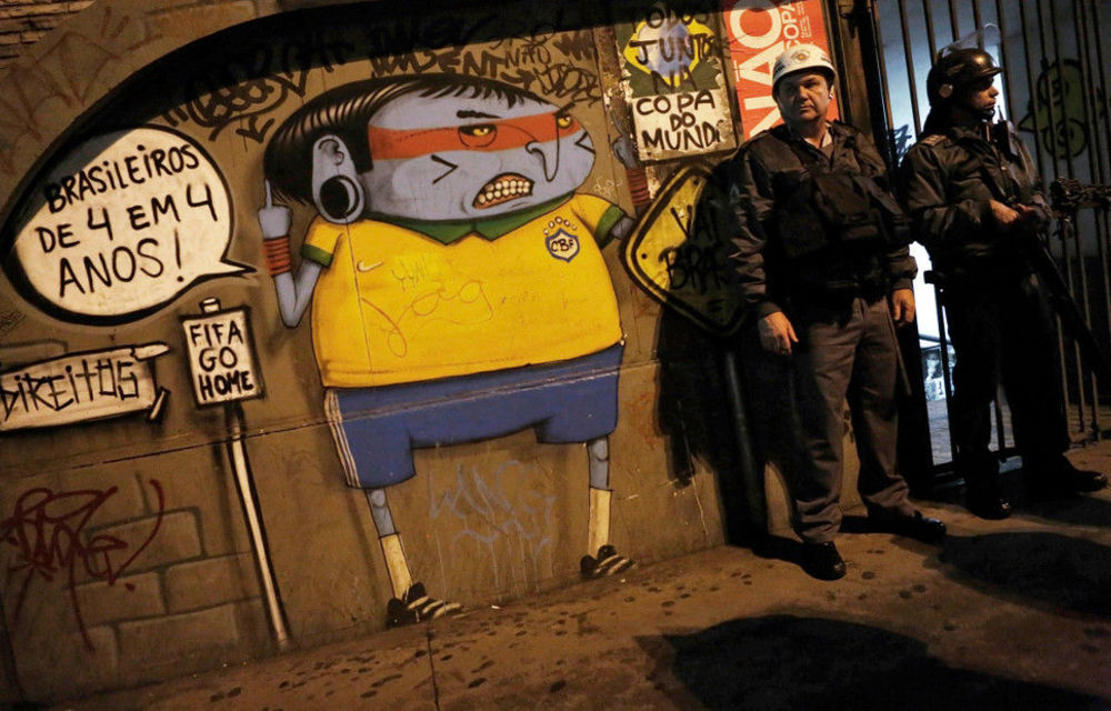 Military police stand next to a mural of an Amazonian tribe member wearing a football jersey during a protest against the 2014 World Cup in São Paulo.