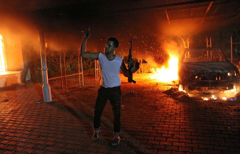 A man waves his rifle as cars and buildings burn in the US consulate compound in Benghazi.