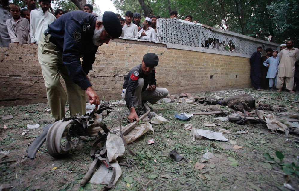 Policemen survey the site of a bomb attack outside a shrine in Peshawar on Thursday June 21