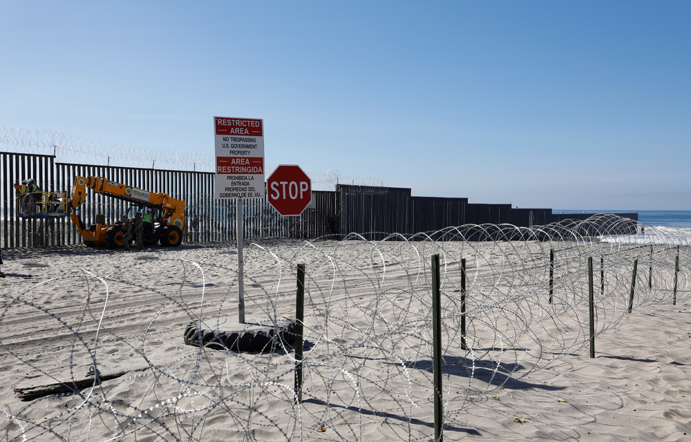 Workers on the U.S. side install concertina wire along the border fence between Mexico and the United States at Border State Park in San Diego