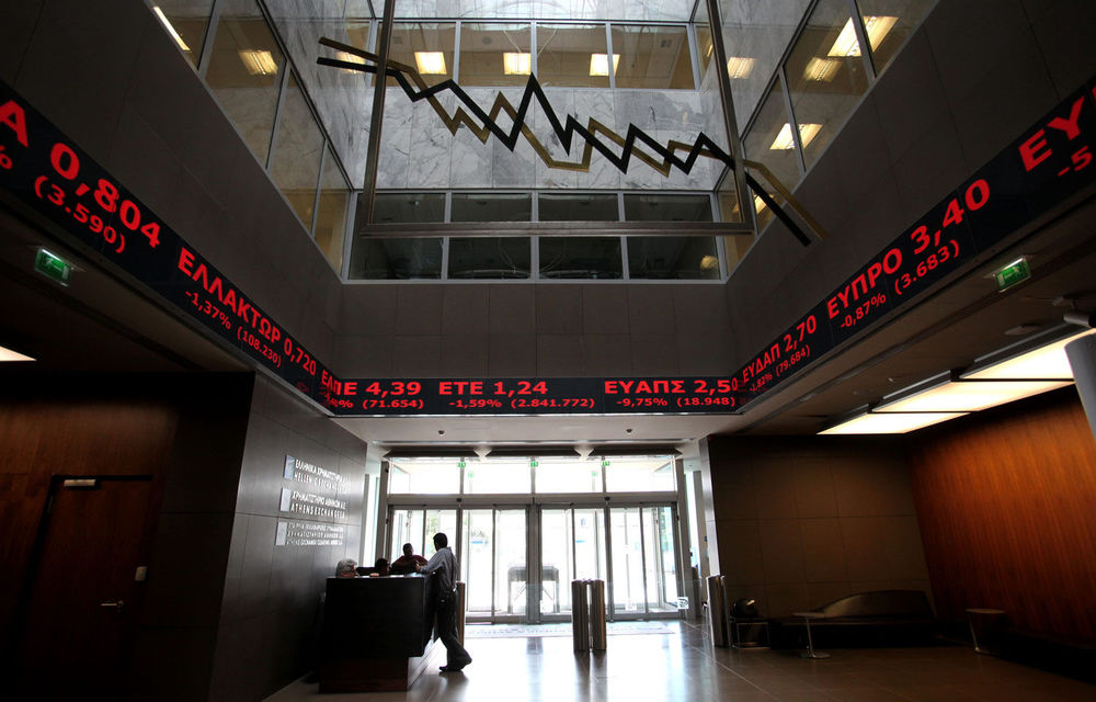 Employees chat under screens showing falling stocks at the Athens Stock Exchange.