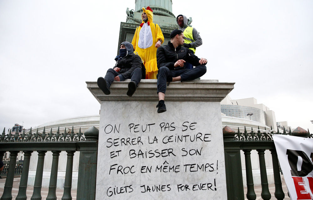 Protesters wearing yellow vests sit at the Place de la Bastille. Message reads