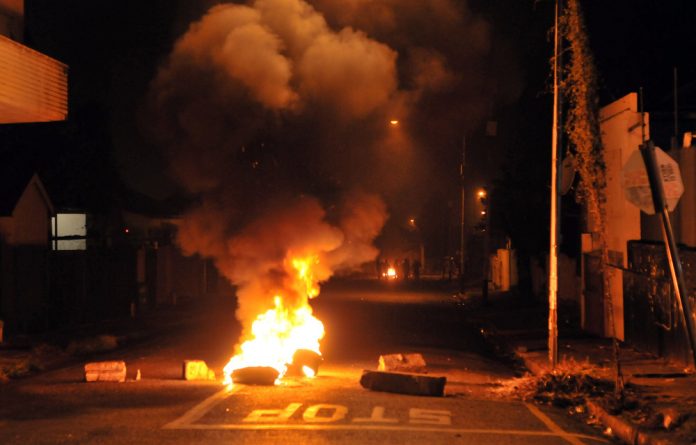 Rioters retreat down a side street after setting fire to tyres near Jules Street in Jeppestown during running battles with the police through out the night on April 17.