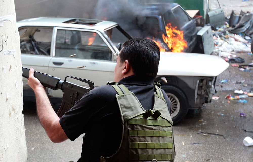 A Sunni gunman fires in a front of burned car during a clashes