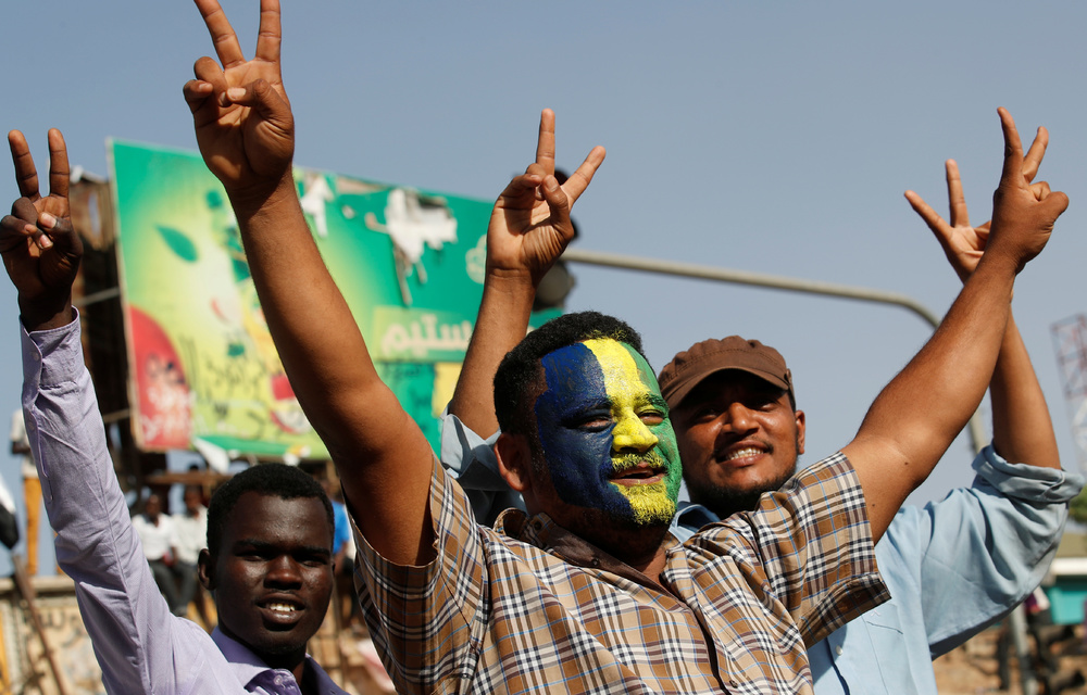 Sudanese protesters make victory signs outside the defence ministry compound in Khartoum